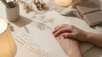 Hands creating botanical art with dried flowers and natural materials on textured paper in warm sunlight for creative design projects.