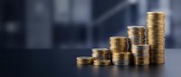Golden coins stacked in ascending order creating growth chart pattern on dark surface with blurred office background for financial success concepts.