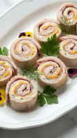 Sliced pinwheel sandwiches with ham and cheese filling arranged on white plate, garnished with fresh parsley and edible flowers for catering and appetizer presentations.