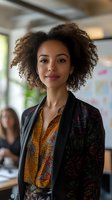 Professional African American businesswoman with curly hair in modern office environment wearing colorful patterned blazer and shirt for corporate presentations.