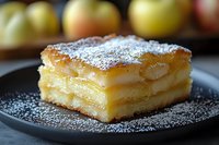 Layered apple cake slice with powdered sugar on dark plate, fresh apples in background, homemade dessert for bakery menu and recipe content.