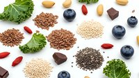Superfood ingredients collection with kale, blueberries, chia seeds, quinoa, flax seeds, goji berries, almonds and dark chocolate on white background.
