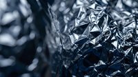 Crumpled aluminum foil texture with metallic reflective surface creating abstract patterns and shadows for modern design projects.