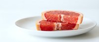 Sliced grapefruit on white plate with fresh citrus segments for breakfast, healthy eating, nutrition, and food styling purposes.