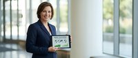 Professional businesswoman in navy suit presenting tablet with data analytics dashboard in modern office environment for corporate presentations.