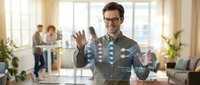 Young Caucasian businessman in glasses interacting with futuristic holographic interface in modern office workspace with colleagues in background.