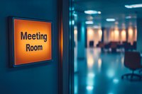 Meeting room sign on office wall with blurred modern corporate interior in blue tones. Empty conference space visible through glass door. Business concept.