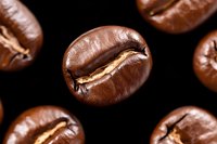 Macro shot of roasted coffee beans scattered on black background showing detailed texture and rich brown color. Perfect for cafe and restaurant marketing.