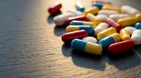 Colorful pharmaceutical capsules and pills scattered on wooden surface with warm lighting for medical healthcare and medication concepts.