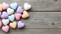 Colorful pastel heart-shaped candies scattered on rustic wooden background with copy space for Valentine's Day, wedding, romance and love themes.