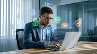 Professional businessman working on laptop with digital security icons and cyber protection interface in modern office environment for technology presentations.