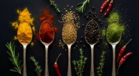 Colorful spices and herbs arranged in wooden spoons on dark background. Turmeric, paprika, cumin, peppercorns and dried herbs for cooking and seasoning.