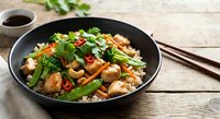 Asian stir-fry with mixed vegetables, mushrooms and herbs in black wok pan on wooden table with chopsticks and soy sauce for healthy cooking.