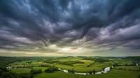 Dramatic stormy sky with dark clouds looming over lush green rolling countryside and winding river, suitable for weather, nature, and landscape design projects.