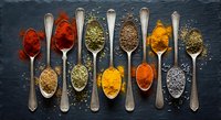 Colorful spices and herbs arranged in wooden spoons on dark slate background. Cooking ingredients including turmeric, paprika, cumin for culinary recipes.