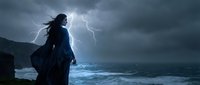 Woman silhouette standing on rocky cliff during dramatic thunderstorm with lightning bolts over turbulent ocean waves under dark stormy clouds at night.