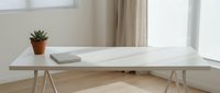 Minimalist white desk with trestle legs in bright modern home office workspace featuring small potted plant and notebook for productivity and remote work.