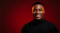 Young African American man smiling confidently in black turtleneck against red background for business and lifestyle marketing campaigns.