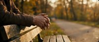 Senior man hands resting on wooden bench in autumn park during peaceful morning walk showcasing relaxation and contemplation in golden fall setting.