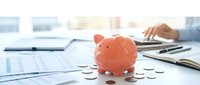 Pink piggy bank surrounded by coins on desk with financial documents and calculator, representing savings, budgeting and personal finance planning concepts.