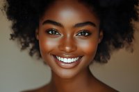 Young African American woman with natural curly afro hair and bright white smile against neutral background, close up portrait showing genuine joy and confidence.