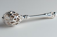 Ornate silver spoon with intricate filigree pattern forming decorative spherical cage at bowl end, displayed on neutral gray background. Luxury tableware design.