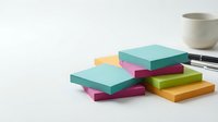 Stacked colorful sticky notes in teal, pink, yellow, and green arranged on white surface with pen and cup, suitable for office and organizational design projects.