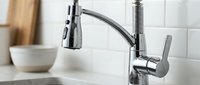 Modern chrome kitchen faucet with pull-out spray head in contemporary home interior. Sleek single handle design for cooking and cleaning tasks.