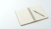 Open spiral notebook with lined pages and silver pen on white background for office planning and note-taking tasks.