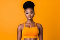 Young African American woman with natural hair in orange sports bra against vibrant orange background, confident athletic portrait showing wellness and strength.