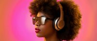 Young Black woman with afro hair wearing gold headphones and sunglasses against vibrant pink background, music and lifestyle concept.