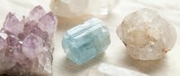 Natural healing crystals collection featuring amethyst cluster, aquamarine and clear quartz specimens on neutral fabric for wellness and meditation practices.