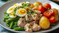 Fresh nicoise salad with tuna, boiled eggs, green beans, cherry tomatoes and potatoes on white plate. Healthy Mediterranean meal for lunch or dinner.