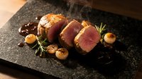Seared beef tenderloin steak slices with golden crust served on black slate plate with roasted garlic, fresh rosemary and rich sauce for gourmet dining.