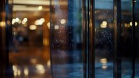 Raindrops on glass window with blurred city lights creating atmospheric bokeh effect at dusk, moody urban scene with reflections and warm glow.