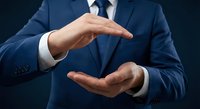 Professional businessman in navy suit making protective gesture with cupped hands against dark background for business insurance and security concepts.