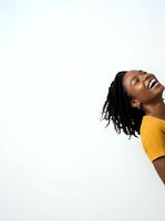 Young African woman with braided hair wearing yellow sweater, laughing joyfully with head tilted back against white background, expressing happiness and positivity for lifestyle and wellness content.