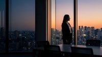 Young professional woman in business attire standing by floor-to-ceiling windows overlooking city skyline at sunset, contemplating urban landscape from high-rise office building.