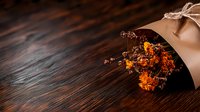 Dried orange flowers spilling from kraft paper bag onto rustic wooden surface, perfect for autumn crafts, floral arrangements, and natural decoration projects.