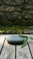 Stacked zen stones with green bamboo leaf on rustic wooden surface, blurred stone wall background, evoking calm, balance, and spa wellness.