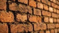 Close-up view of weathered red brick wall with aged mortar joints showing rustic texture and warm earthy tones for construction and architectural backgrounds.