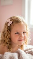 Adorable young blonde girl with curly hair and pink bow smiling warmly in soft natural light. Sweet childhood portrait for family and parenting content.