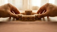 Hands arranging wooden blocks with gear mechanisms on desk surface for business strategy and problem-solving concepts in office environment.
