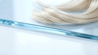 Blonde hair strand with blue glass rod on white background for hair styling and beauty salon treatments.