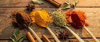 Colorful aromatic spices and herbs arranged in wooden spoons on rustic table. Turmeric, paprika, coriander seeds, cinnamon sticks for cooking and seasoning.