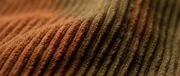 Close-up macro shot of ribbed corduroy fabric texture showing detailed weave pattern in warm brown and orange tones for textile and fashion design projects.