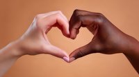 Diverse hands forming heart shape against warm brown background, symbolizing unity, love, acceptance and racial harmony in modern society.