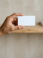 Male hand holding blank white business card against blurred neutral background, suitable for branding, corporate identity, and marketing mockup designs.