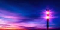 Telecommunications tower with glowing pink lights against dramatic sunset sky featuring vibrant purple and blue clouds in panoramic view. Suitable for technology concepts.
