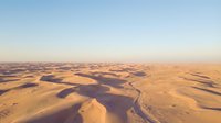 Aerial view of vast desert landscape with golden sand dunes and winding paths at sunset, suitable for travel and nature backgrounds.